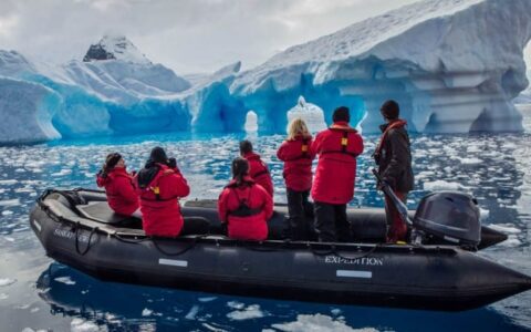 Guests from the spirit of shackleton expedition cruise sit in a zodiac with icebergs in the distance, at antarctica
