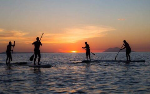 A group of people on stand up paddleboards on the ocean during a sunset in indonesia