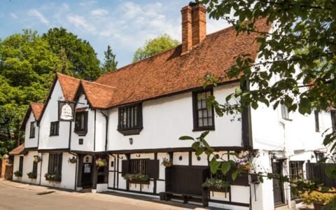 A white-&-brown Tudor Mansion with terracotta roof tiles, seen on a sunny day during a London river cruise.