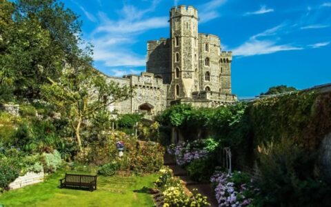 Immaculate gardens leading up to tall Windsor Castle, seen on a sunny day during the Classic England River Thames Cruise.