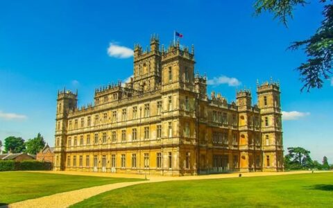 Highclere Castle with 3 stories, flags flying, green grass surrounding & blue sky, seen during a barge cruise in England.