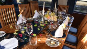 10-guest dining table set for dinner with white linens, candles, flowers & wine glasses aboard River Thames barge Magna Carta.