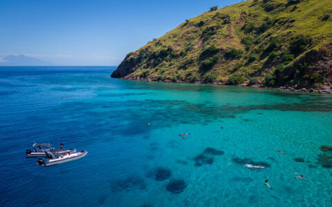 2 small tender boats sit at edge of turquoise sea as guests on Aqua Blu Raja Ampat Cruise snorkel beside bright green mountains.
