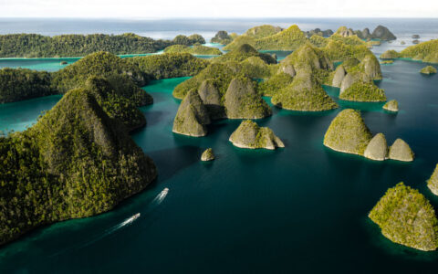 Aerial view of 2 tender boats cruising in turquoise water among gumdrop green islands on the Aqua Blu Raja Ampat Cruise.