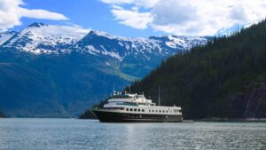 Small ship Chichagof Dream cruising past snowy mountain ranges in alaska.