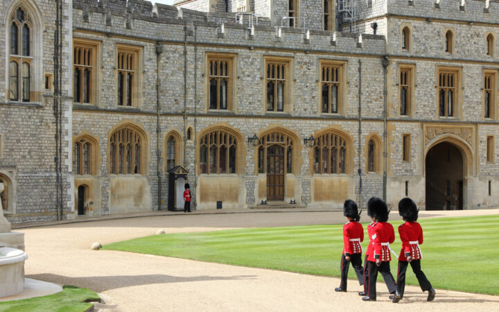 Royal guards in tall black furry hats, black pants & red coats approach Windsor Castle during the Classic England River Thames Cruise.
