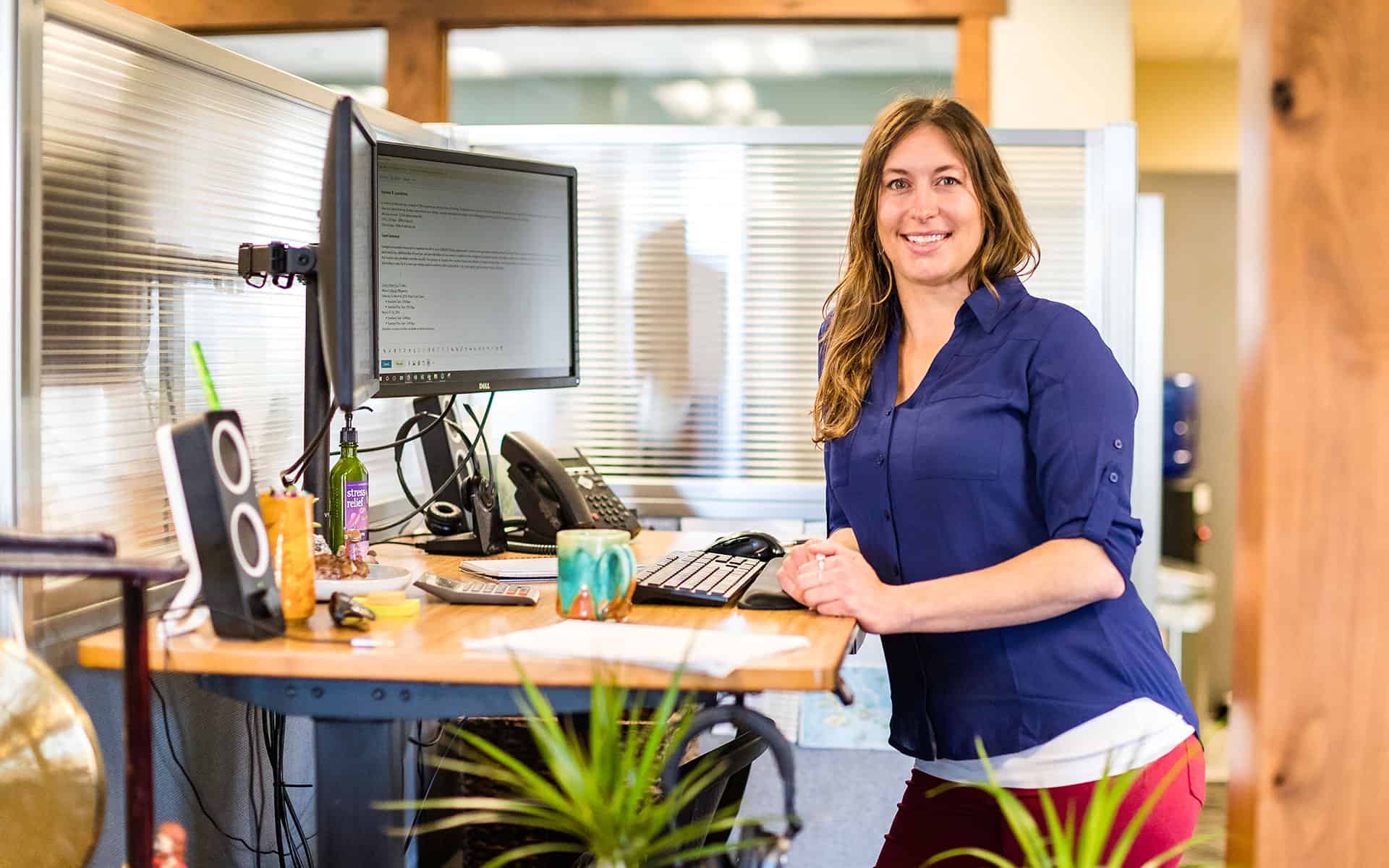 smiling adventuresmith explorations staff member in a purple shirt standing at a computer with plants around her desk