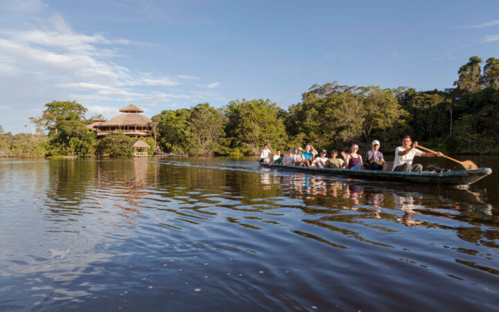 Dugout canoe full of Ecuador Amazon Adventure travelers moves through calm waters surrounded by lush rainforest on a sunny day.