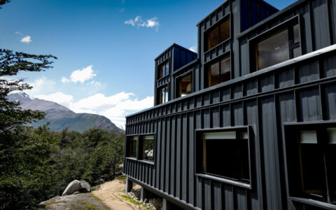 Dark steely exterior of a modern lodge with tall windows sitting beside a tree on the Explora Connects El Chaltén trip.