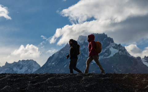2 Explora Connects Torres del Paine guests hike over a rocky hilltop with a snowcapped peak in the distance.