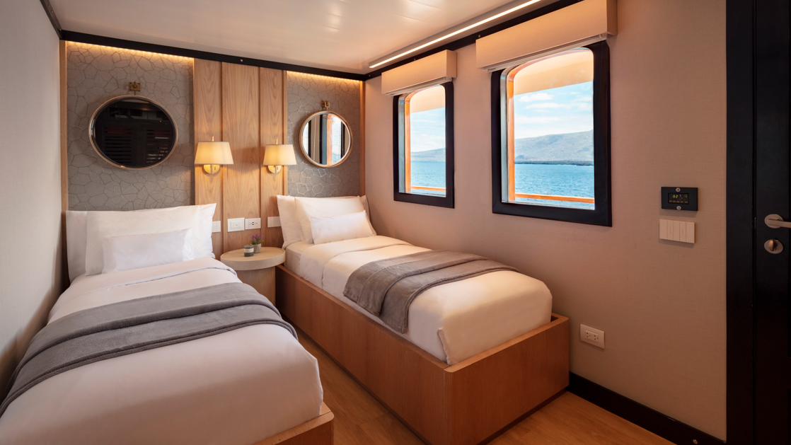 Historic wooden Twin Suite with white sheets with a shared bedside table and two large windows looking out at the ocean