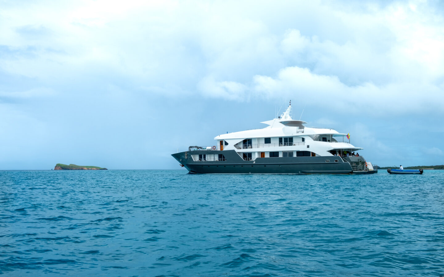 White and grey Small ship infinity anchored in the Galapagos on a cloudy day next to a small island