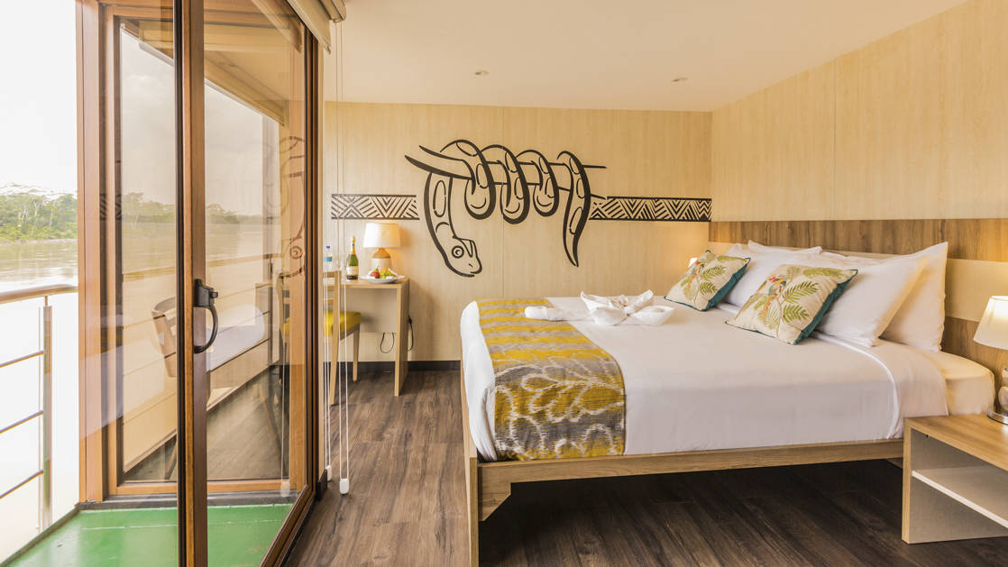 Manatee Amazon Explorer Deluxe Cabin with king bed, private balcony, sliding glass door, nightstand, reading lights and desk.
