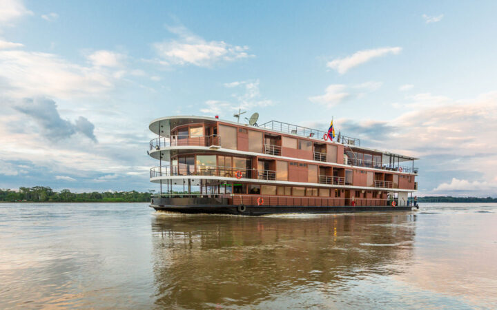 Manatee Amazon Explorer small ship with 4 guest decks including open-air trop deck, in copper color, cruising the River.