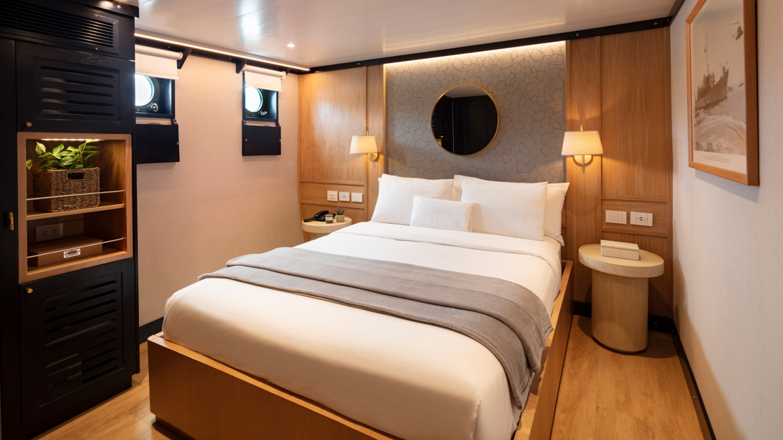 Large bed with white bedding and flanked by nightstands featuring two portholes and a large historic photograph of the Grace