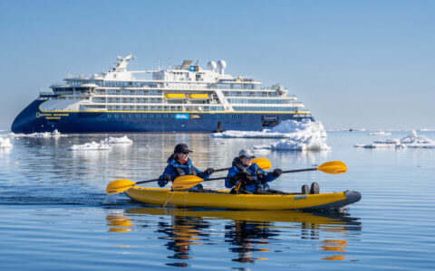 Kayakers explore the icy waters off the national geographic expedition ship ship that is shown behind them.