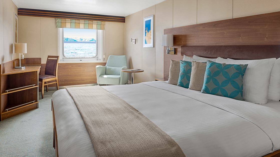 A large double bed and window are featured in this category 3 cabin with warm wood aboard the National Geographic Explorer