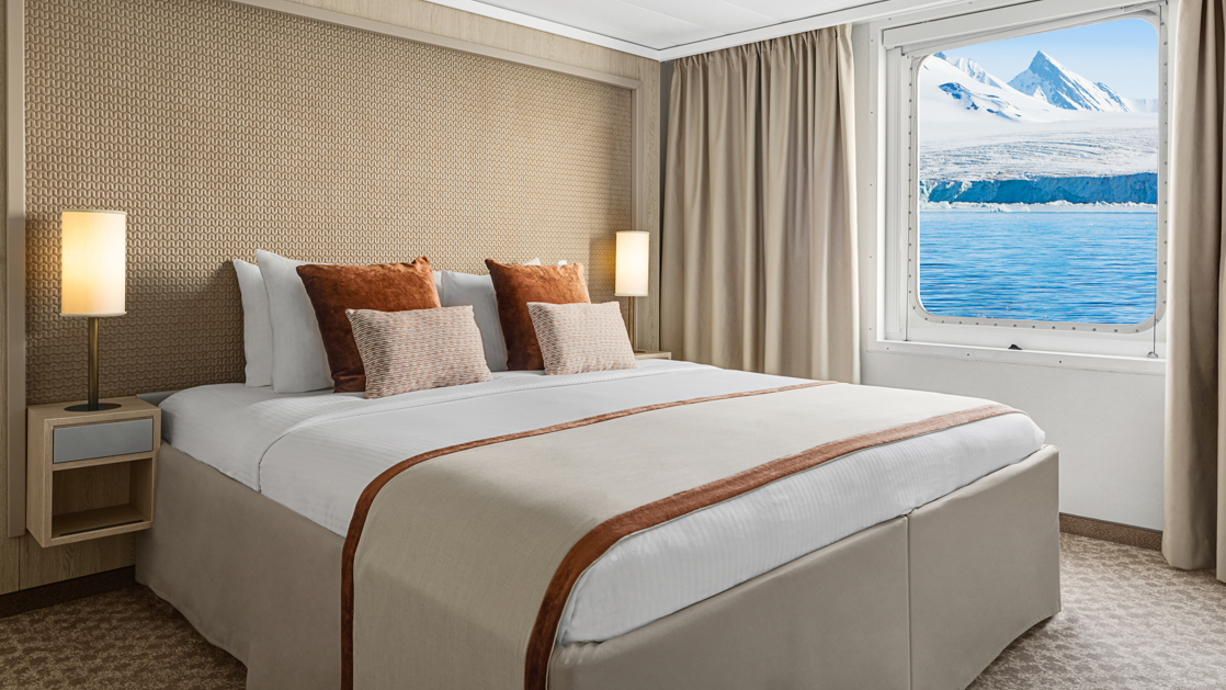 A large double bed and window are featured in this category 4 cabin with warm wood aboard the National Geographic Explorer