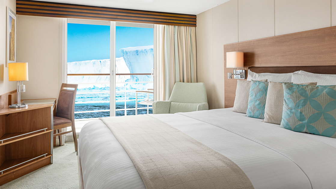 A large double bed and balcony are featured in this category 5 cabin with warm wood aboard the National Geographic Explorer