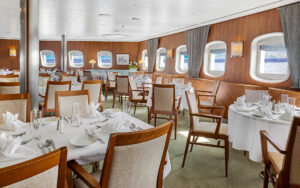A beautiful dining room featuring handsome wood trim and white linen service aboard the National Geographic Explorer awaits