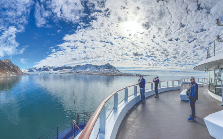 Travelers admiring Svalbard's Arctic mountains from the bow of a small expedition cruise ship.