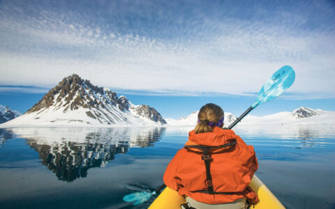 A traveler kayaks toward snow-covered peaks on an Arctic expedition cruise.