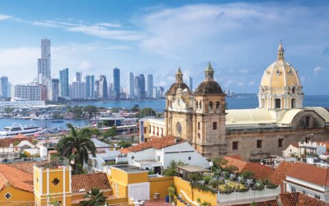 Aerial view of Cartagena, Colombia, with modern high-rise buildings and colorful Caribbean buildings including a church.