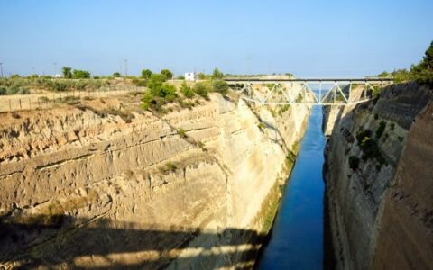 a canal runs between dirt slopes in corinth, leading to the aegean sea