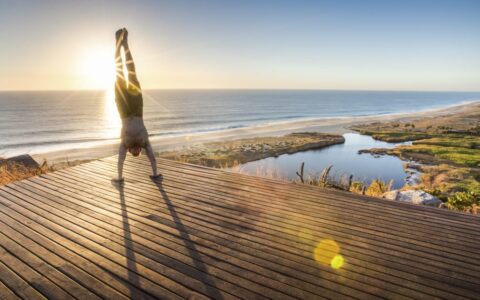 person doing a yoga hand stand on a platform above the beach during the sunset