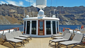 top deck of small cruise ship with lounge chairs in front of rocky landscape and blue waters on a sunny day