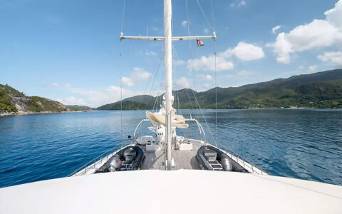 View from upper deck of large white sailboat in Caribbean with sails furled & 2 Zodiac boats sitting on teak deck near bow