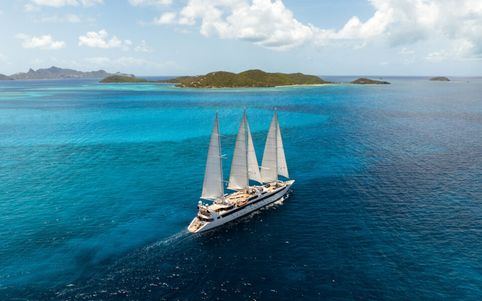 Aerial view of Le Ponant white sailing ship with 3 masts cruising through turquoise sea on a sunny day in the Caribbean.