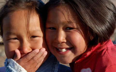 2 Inuit girls laugh & smile, seen on Le Commandant Charcot Inuit Spring in Ammassalik small ship cruise in northeast Greenland.