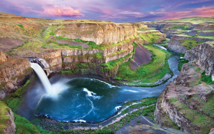 Large waterfall feeds flowing river in green & tan canyon, seen on Pacific Northwest tours.