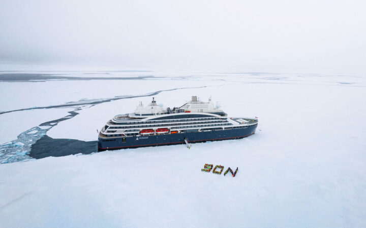 Aerial view of Le Commandant Charcot polar expedition ship stopped in the ice with guests ashore during a Ross Sea expedition.