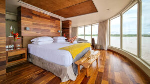 Beautiful wood finishes large wrap around windows featuring large bed chase lounge aboard Delfin III on the Amazon in Peru