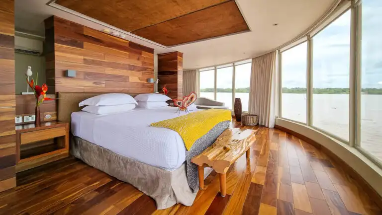 Beautiful wood finishes large wrap around windows featuring large bed chase lounge aboard Delfin III on the Amazon in Peru