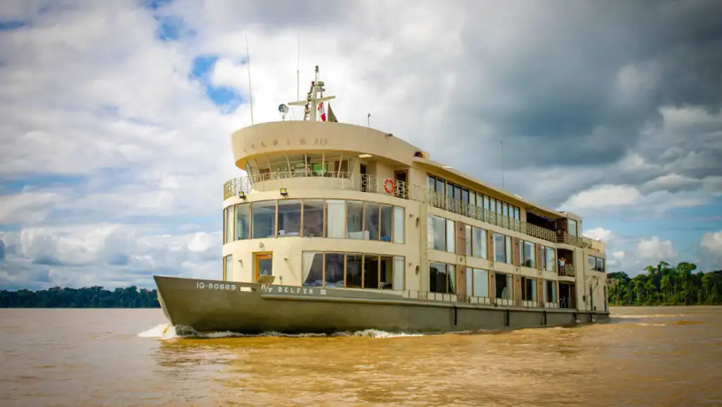 Exterior of bow & port side of Delfin III riverboat with green hull & beige upper decks cruising in the Peruvian Amazon.