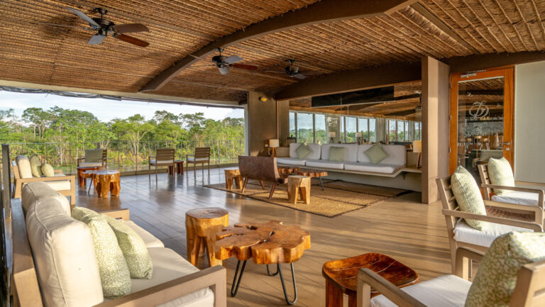 Sun deck terrace of Delfin III Amazon riverboat with open-air lounge with padded white seating, ceiling fans & wood coffee tables.