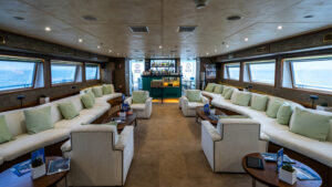 Interior lounge of Harmony G Mediterranean mega yacht with waved white & green bench couches along walls with view windows.