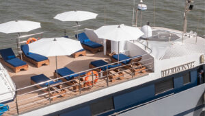 Aerial view of Harmony G Mediterranean mega yacht's teak sun deck with blue chaise loungers & white umbrellas on a sunny day.
