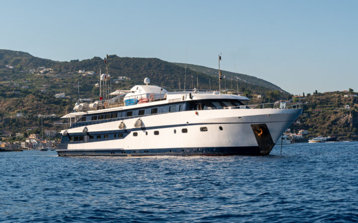 Harmony G white & black mega yacht with 3 guest decks sits at anchor in Mediterranean port on a sunny day.