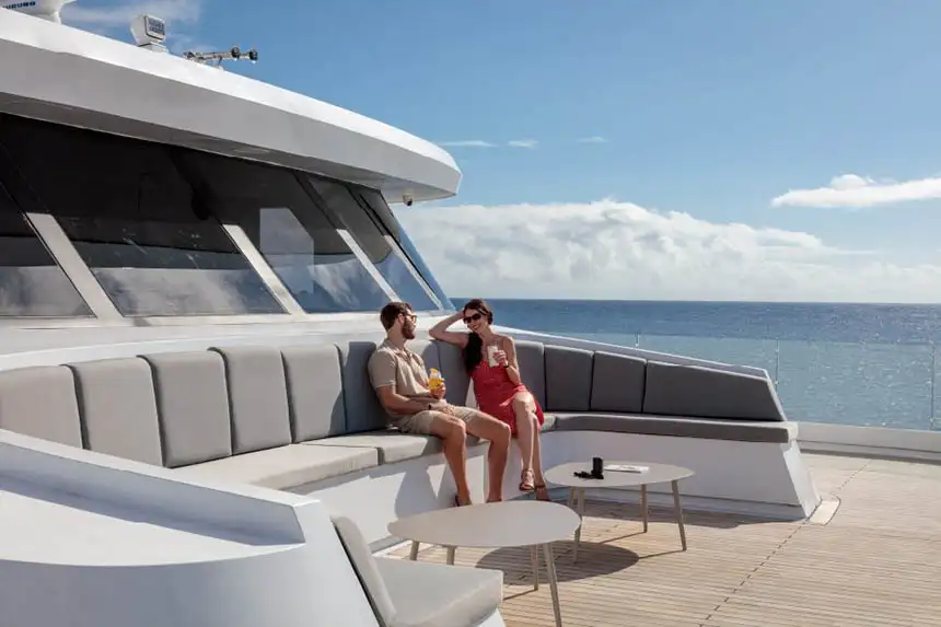 The curved bow bench seating with tables aboard Hermes and a couple sitting with drinks on it