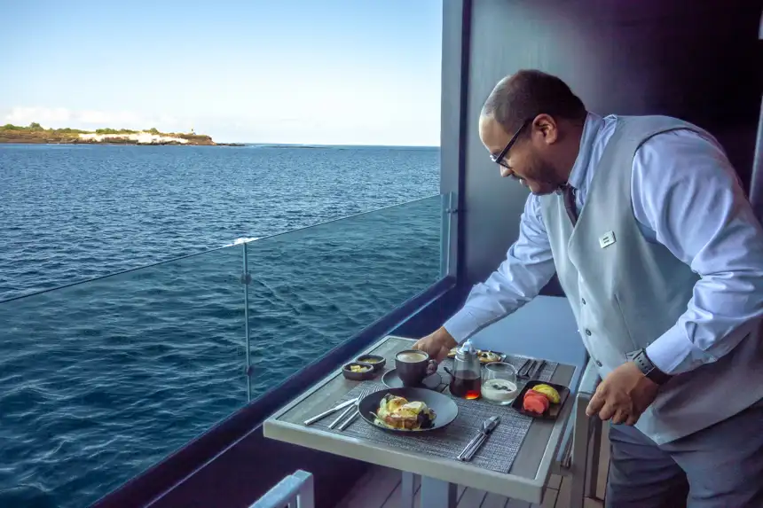 A butler places a latte on a table on the balcony of Hermes catamaran
