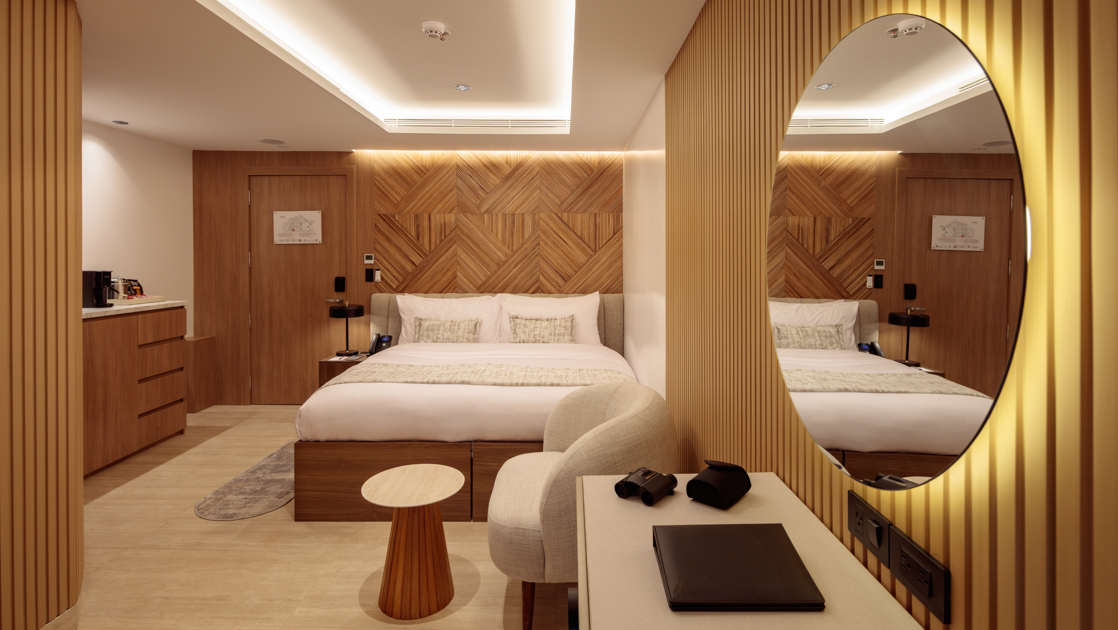 Single Suite with queen bed on Hermes mega-catamaran with white linens, modern furniture, wood accent walls & recessed lighting.