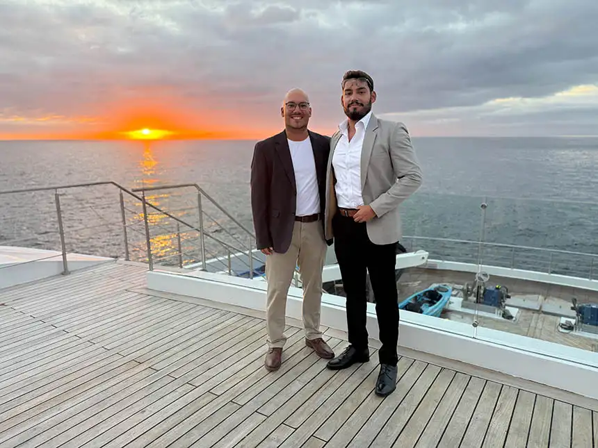Two male Galapagos national park guides dressed up on the bow of Hermes catamaran