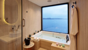 Guest bathroom with stone tub by window, glass-walled rain shower, vanity & dual bowl sinks on Hermes Galapagos catamaran.