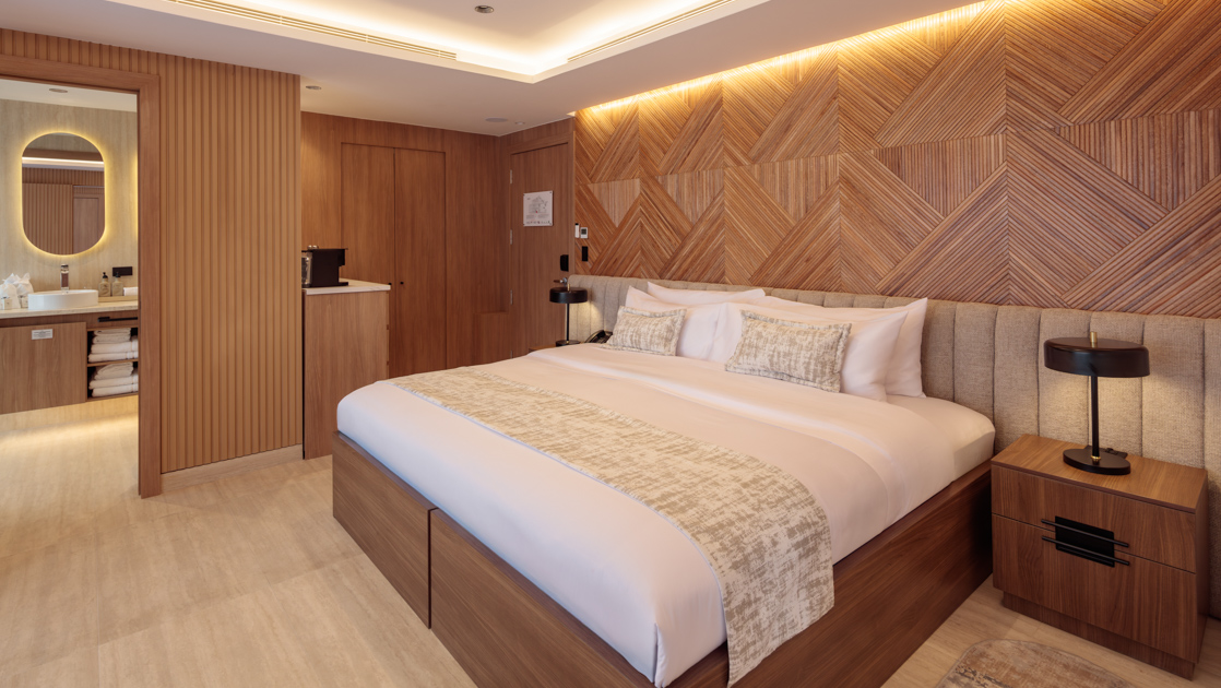 Double Suite with king bed on Hermes mega catamaran with white linens, modern furniture, wood accent walls & recessed lighting.