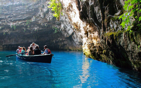 Travelers in a small row boat with a man in a white shirt rowing seen in a cave at Mellisani Lake in Greece with foilage growing on the steep walls