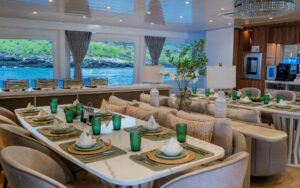 Dining room aboard Monique small yacht. Multiple marble tables set for a meal next to buffet bar and wide viewing windows